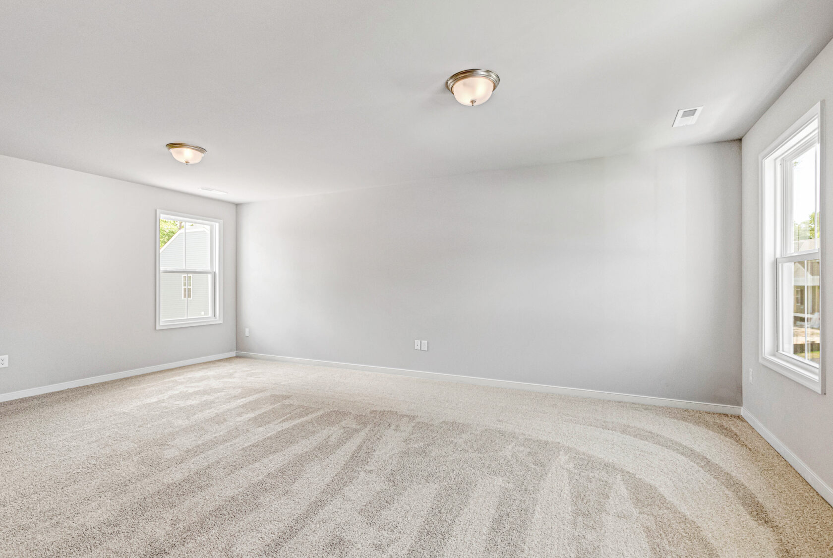 Spacious, empty room with beige carpet, white walls, and two windows in Poplar Village's Lot 28 letting in natural light.