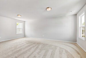 Spacious, empty room with beige carpet, white walls, and two windows in Poplar Village's Lot 28 letting in natural light.