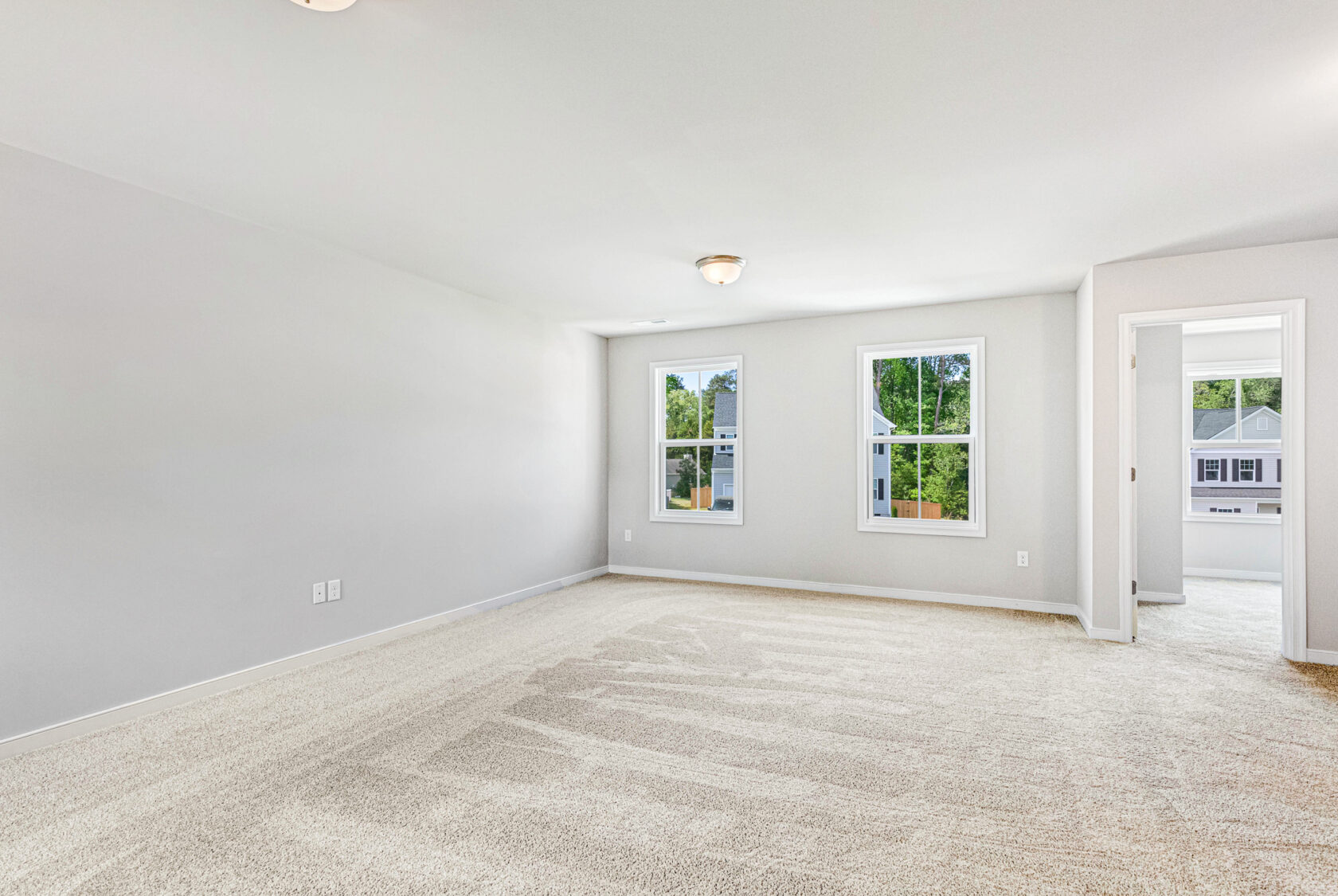 Bright, empty carpeted room with two windows in Lot 28, Poplar Village; white walls and open doorway included.