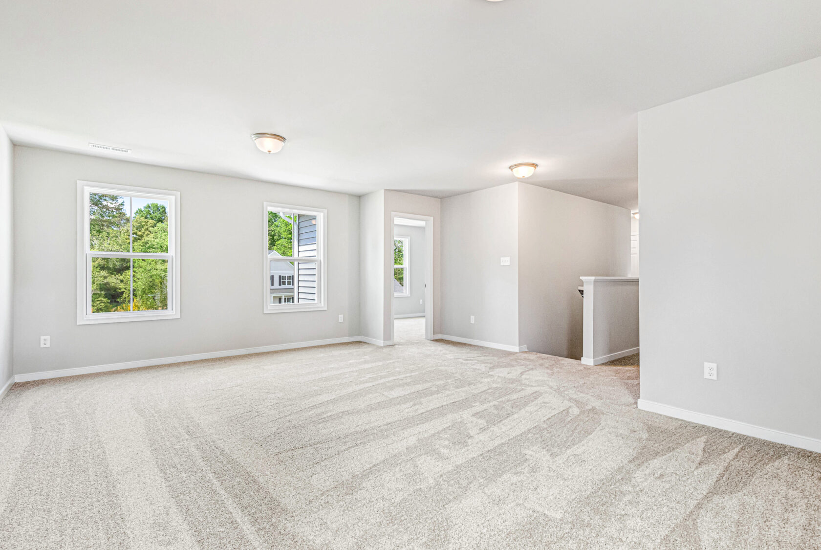Spacious, empty carpeted room in Poplar Village with white walls, large windows, and a door to another area.