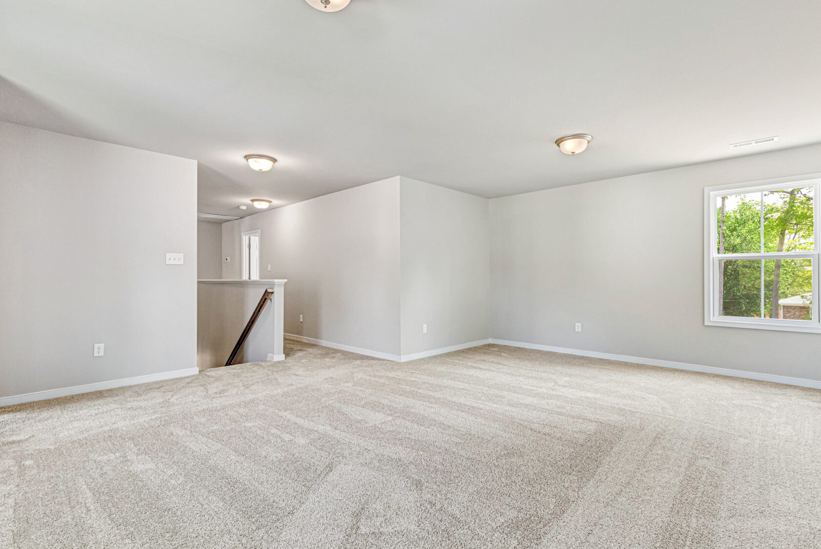Spacious empty room in Poplar Village with beige carpet, white walls, ceiling lights, and natural light.