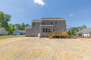 Back view of Lot 28 in Poplar Village: two-story house, small deck, straw-covered yard on a sunny day.