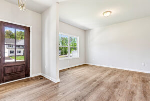 Bright, empty room in Poplar Village with wood floors, white walls, large windows, and a dark wooden front door.