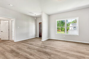 Empty, bright room in Poplar Village with large window, light walls, wooden floor, and views of greenery from Lot 28.