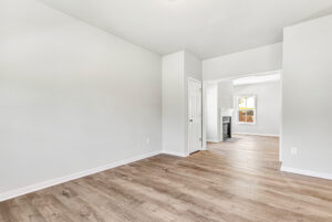 Bright empty room with light wood flooring in Poplar Village, Lot 28, leading to another room with a fireplace.