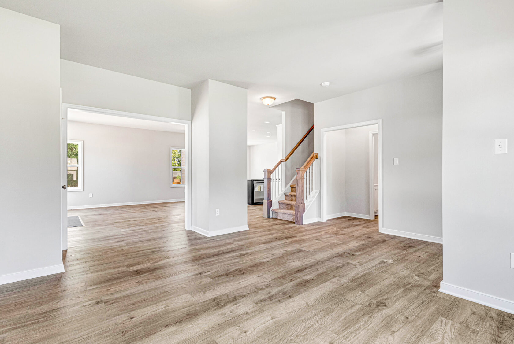 Bright, empty living space in Poplar Village with wood flooring, white walls, and a staircase to the upper floor.