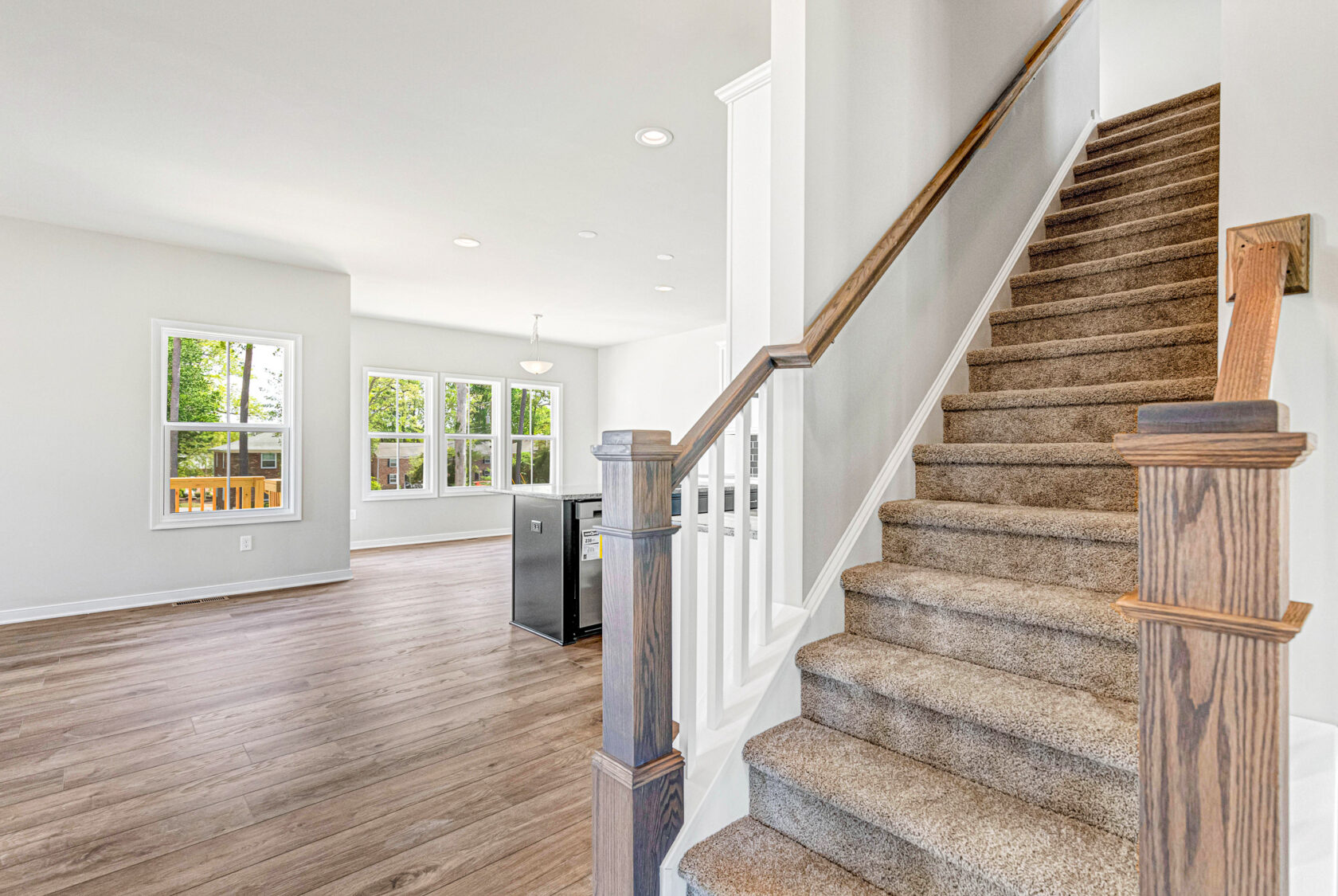 Bright, modern interior in Poplar Village Lot 28 with carpeted stairs, open living area, large windows, and wood flooring.