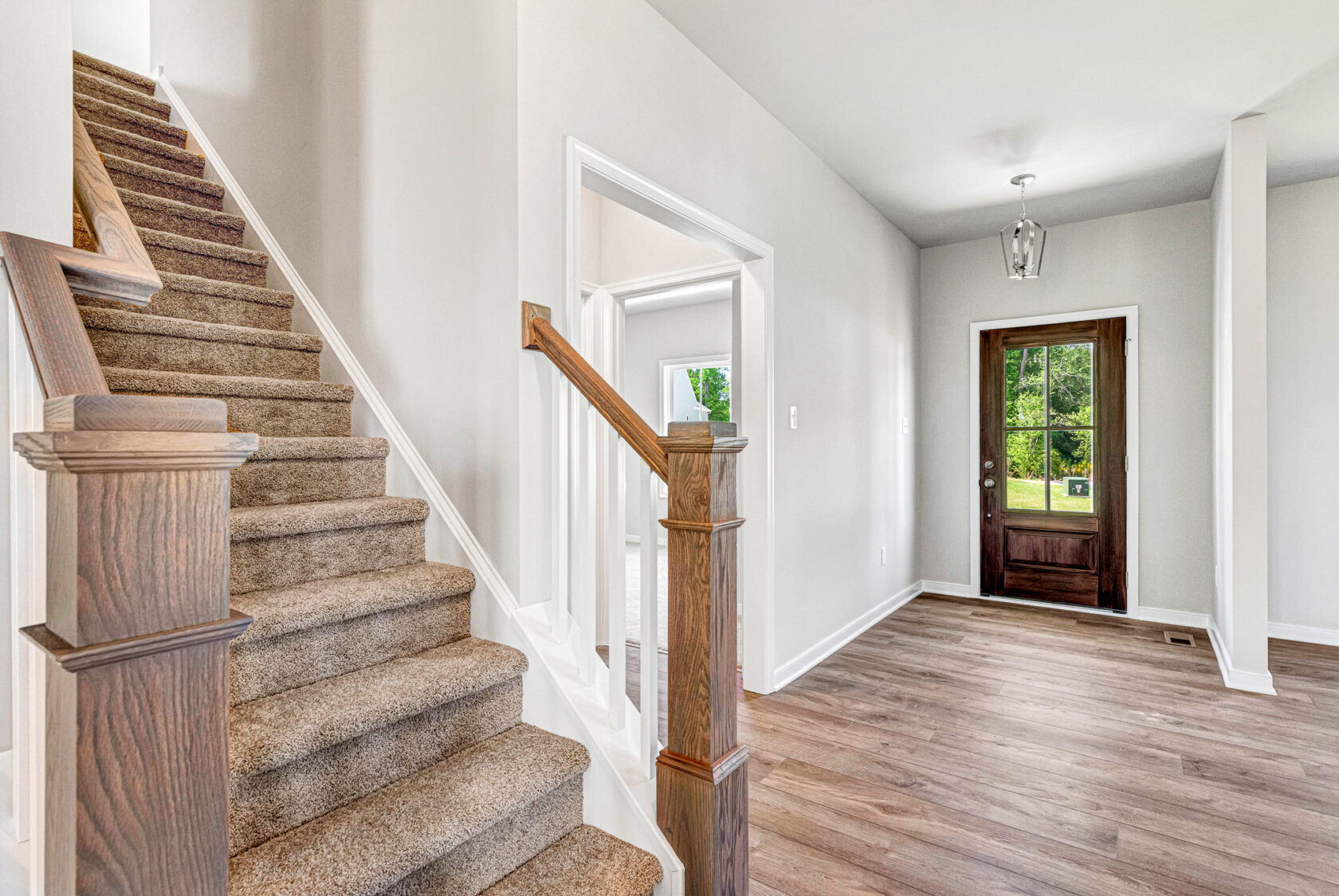Bright Poplar Village entryway with wooden front door, carpeted stairs, and light wood flooring in Lot 28.