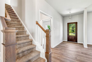 Bright Poplar Village entryway with wooden front door, carpeted stairs, and light wood flooring in Lot 28.