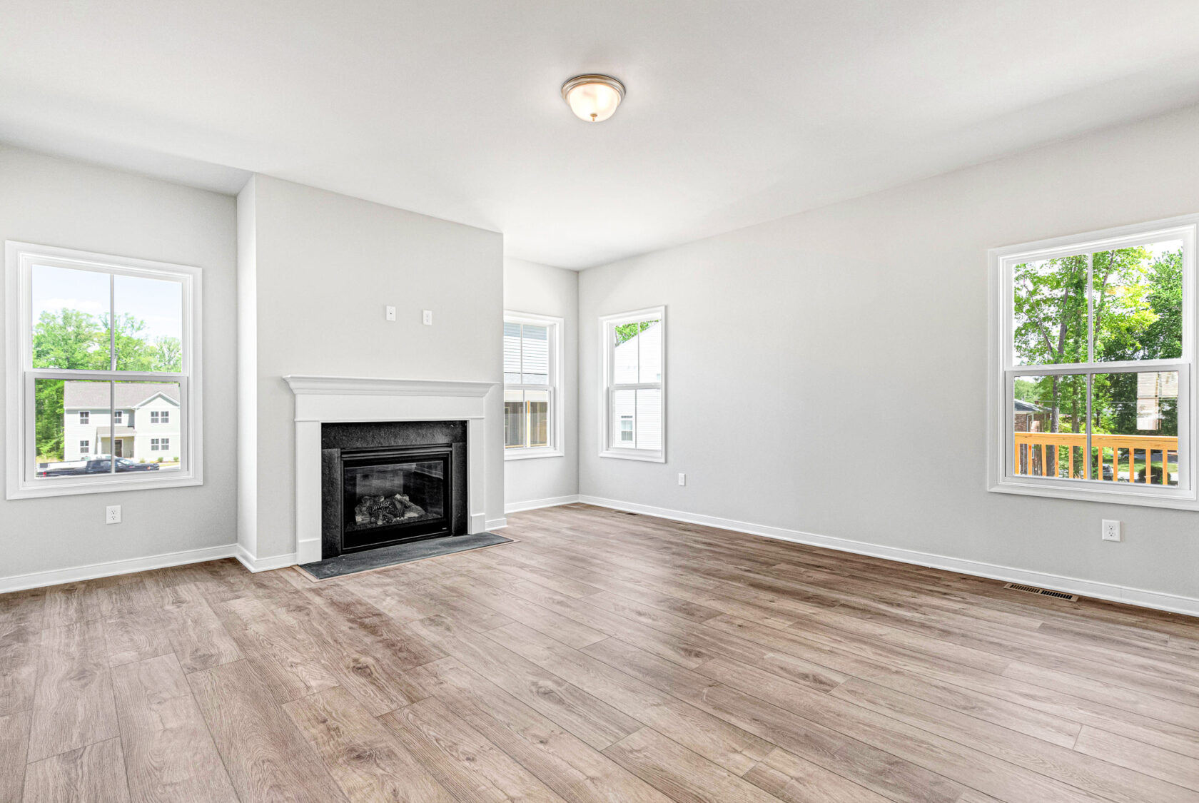 Bright, empty living room with wood floors in Poplar Village, Lot 28; fireplace and large windows let in natural light.