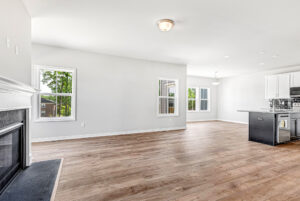 Bright, modern open-concept living room and kitchen with wood floors and large windows in Poplar Village Lot 28.