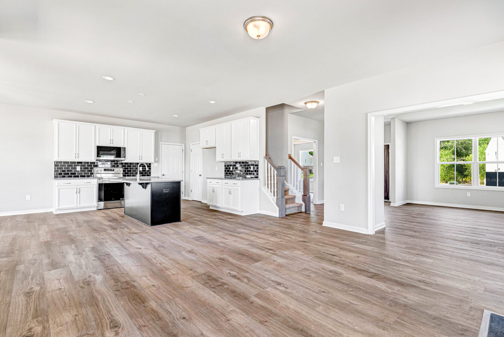 Spacious modern kitchen and living area with wood flooring in Poplar Village, Lot 28; white cabinets, black island.