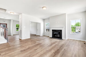 Bright, empty living room with wood floors in Poplar Village Lot 28, fireplace, and large windows with natural light.