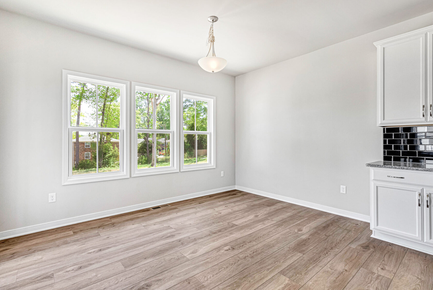 Bright empty room in Poplar Village with large windows, wood flooring, white walls, and a hanging light fixture.
