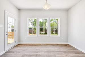 Bright, empty room with wood floors, three large windows, and deck access in Poplar Village's Lot 28.