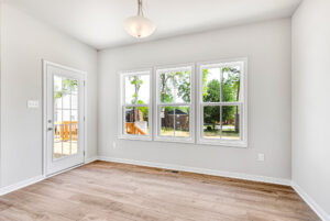 Bright, empty room in Poplar Village with light wood floors, white walls, windows, and a glass door to the deck.