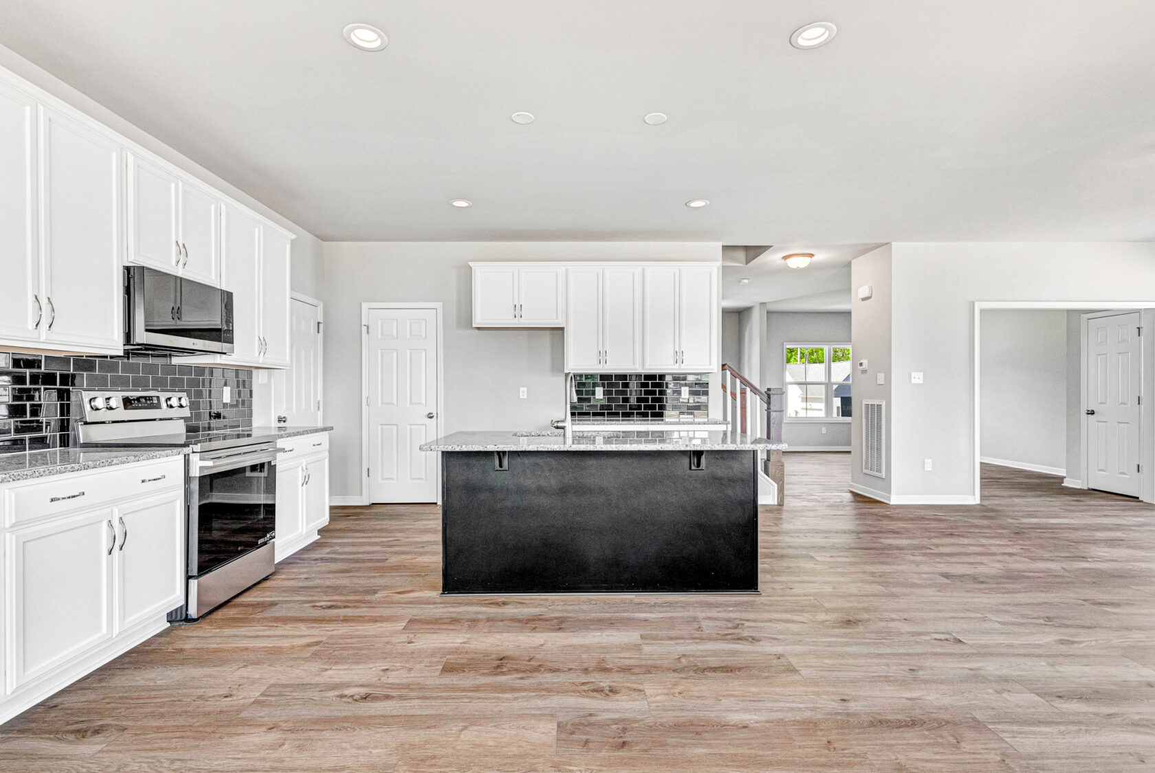 Modern kitchen in Lot 28, Poplar Village features white cabinets, black island, tile backsplash, and wood flooring.