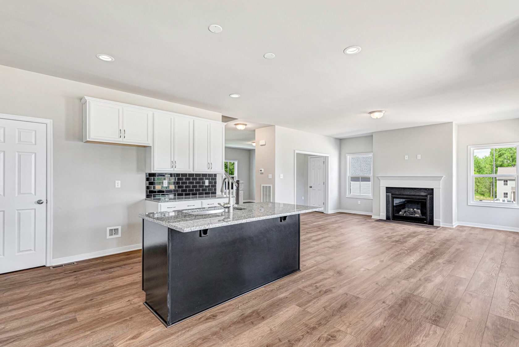 Modern open kitchen in Poplar Village, Lot 28, featuring a black island, white cabinets, wood floors, and fireplace.