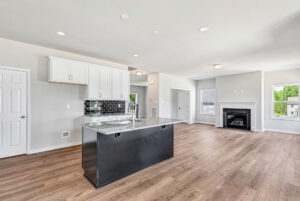 Modern open kitchen in Poplar Village, Lot 28, featuring a black island, white cabinets, wood floors, and fireplace.