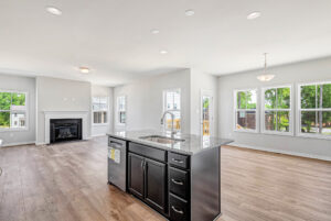 Modern open-plan kitchen and living area at Lot 28, Poplar Village with island, fireplace, large windows, and hardwood floors.