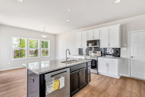 Modern kitchen in Poplar Village with white cabinets, black island, stainless steel appliances, and large windows.
