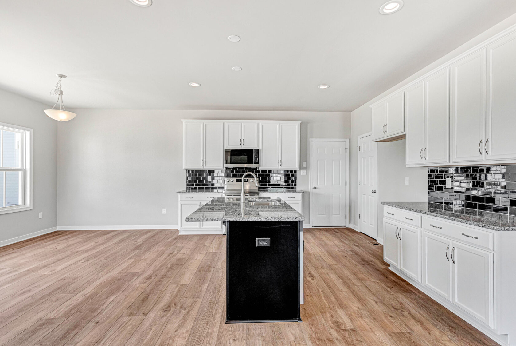 Modern kitchen in Poplar Village, Lot 28—white cabinets, black island, granite counters, and black tile backsplash.