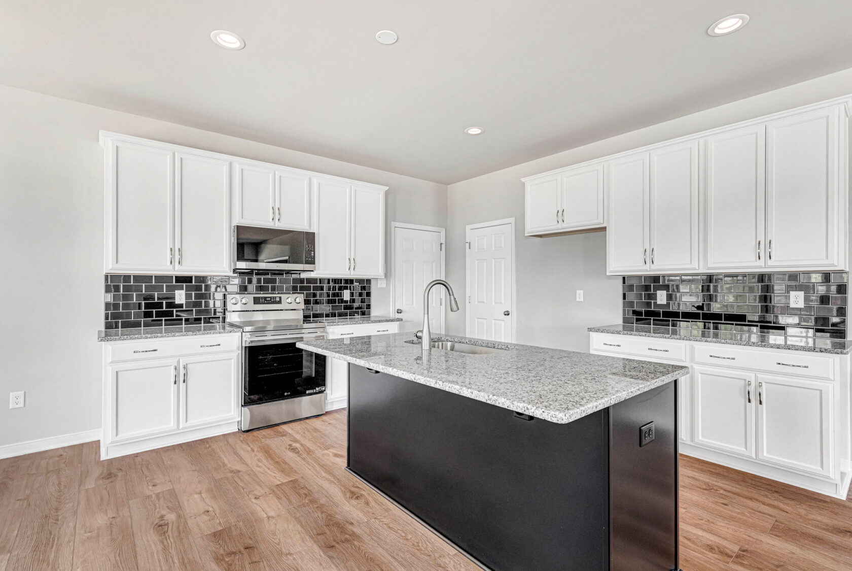 Modern kitchen in Poplar Village with white cabinets, black tile backsplash, granite island, and stainless appliances.