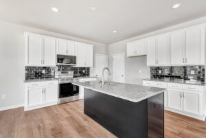 Modern kitchen in Poplar Village with white cabinets, black tile backsplash, granite island, and stainless appliances.
