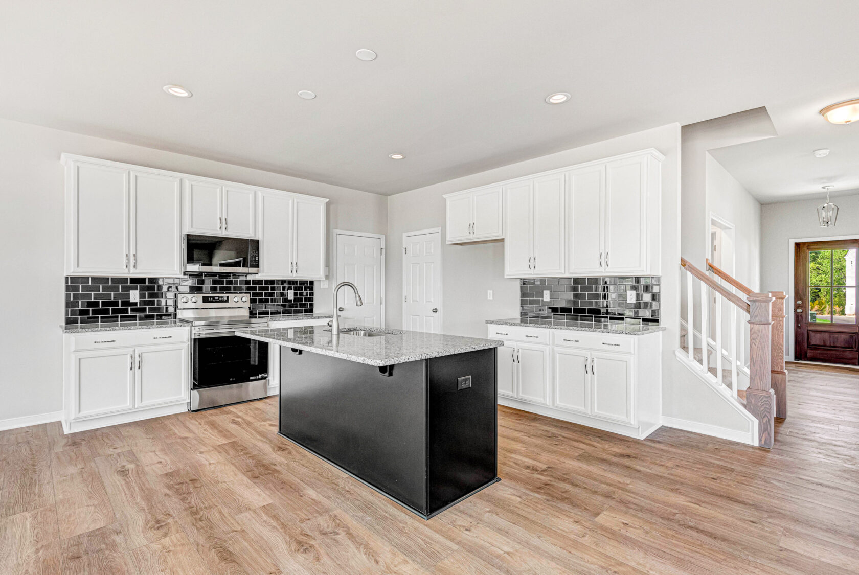 Modern kitchen in Poplar Village, Lot 28, with white cabinets, black backsplash, granite island, and wood flooring.