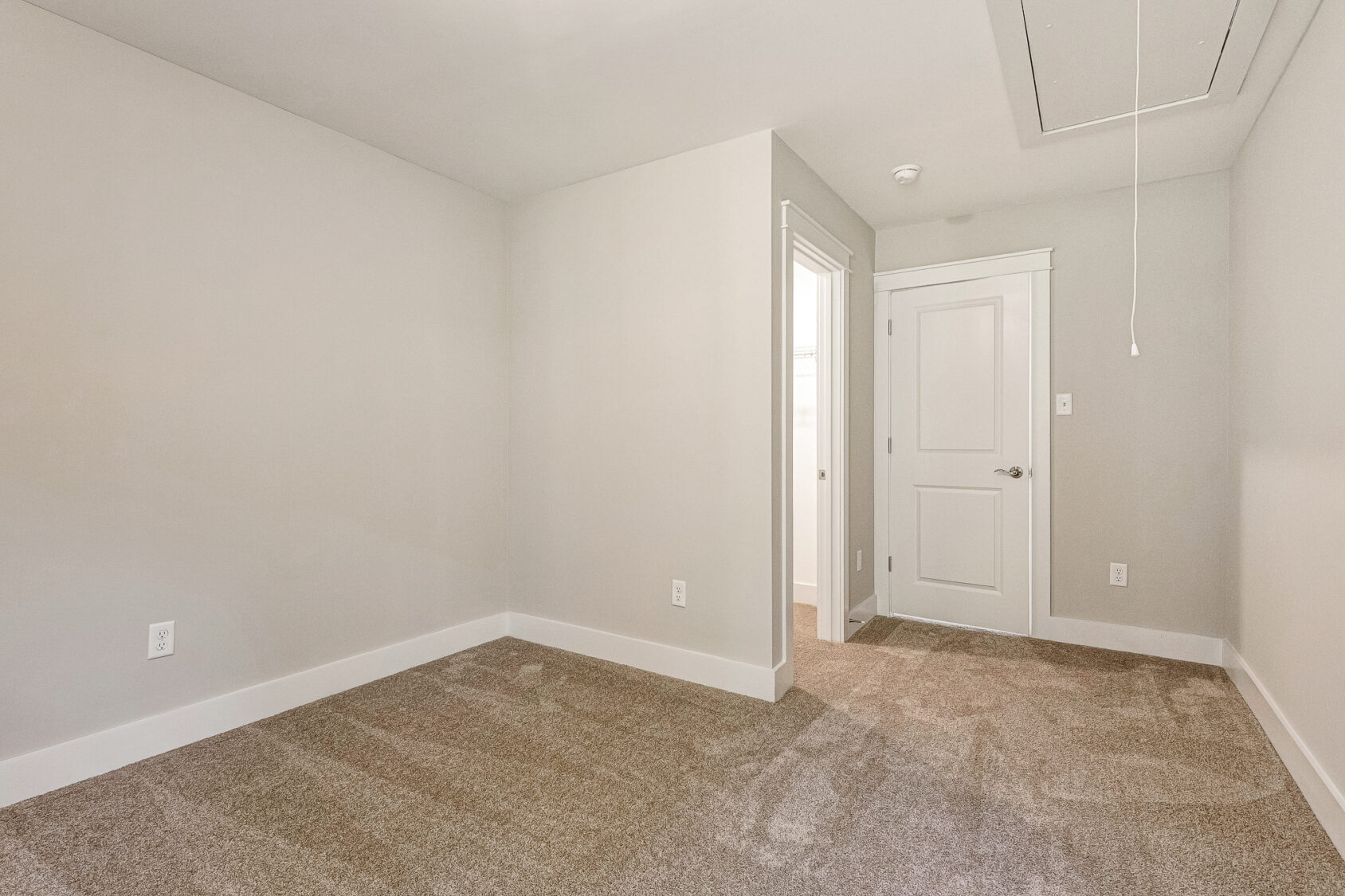 Empty beige carpeted room in Somerset Hill, Lot 7, with white walls, baseboards, door, and ceiling hatch with pull string.