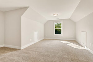 Empty, carpeted attic on Somerset Hill with sloped ceilings, white walls, a window, and doors on opposite sides—Lot 7.