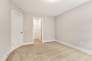 Spacious Somerset Hill Lot 7 room with beige carpet, white trim, two doors, and an open closet with shelving.