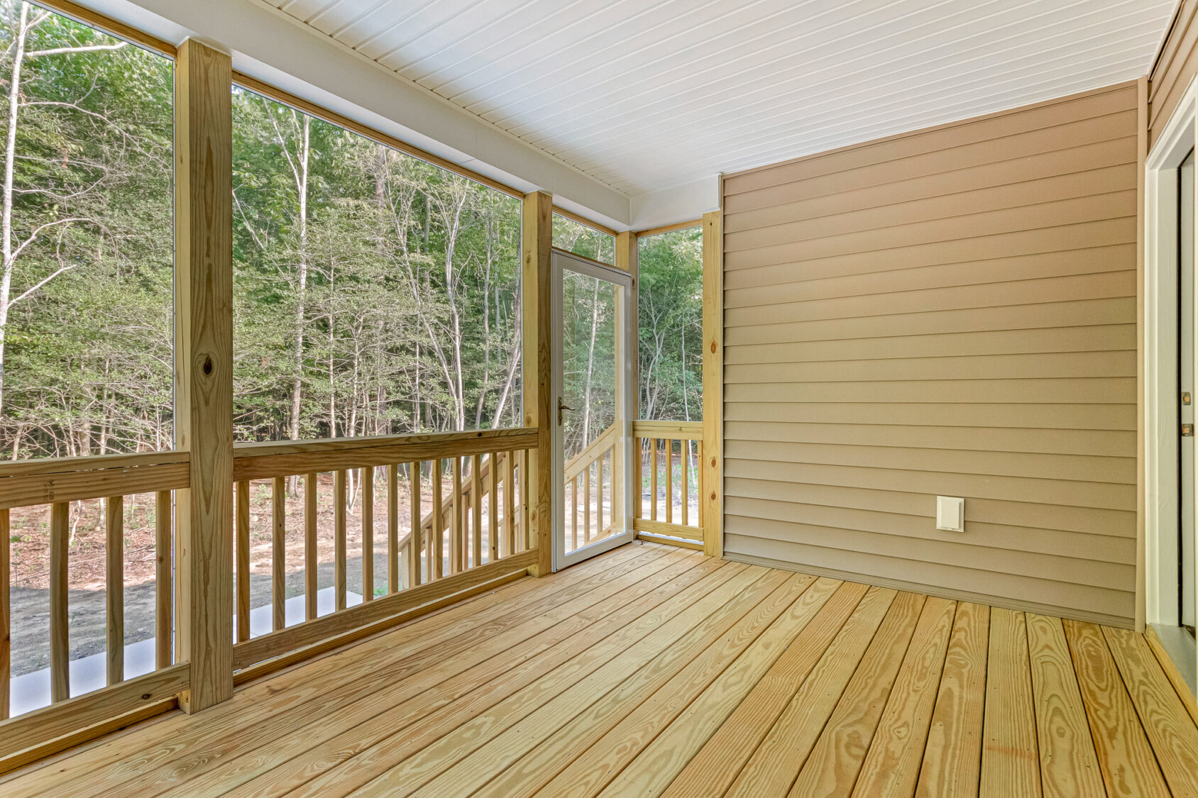 Screened-in wooden porch with railing at Somerset Hill Lot 7, overlooking woods and featuring a door to the outside.
