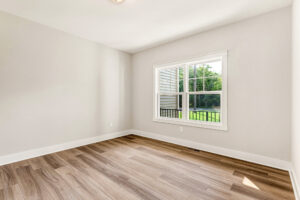 Spacious empty room in Somerset Hill, Lot 7, with light wood floors, cream walls, and a window to a green yard.