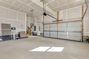 Spacious, empty two-car garage at Somerset Hill Lot 7 with unfinished walls, closed door, and items near the stairs.