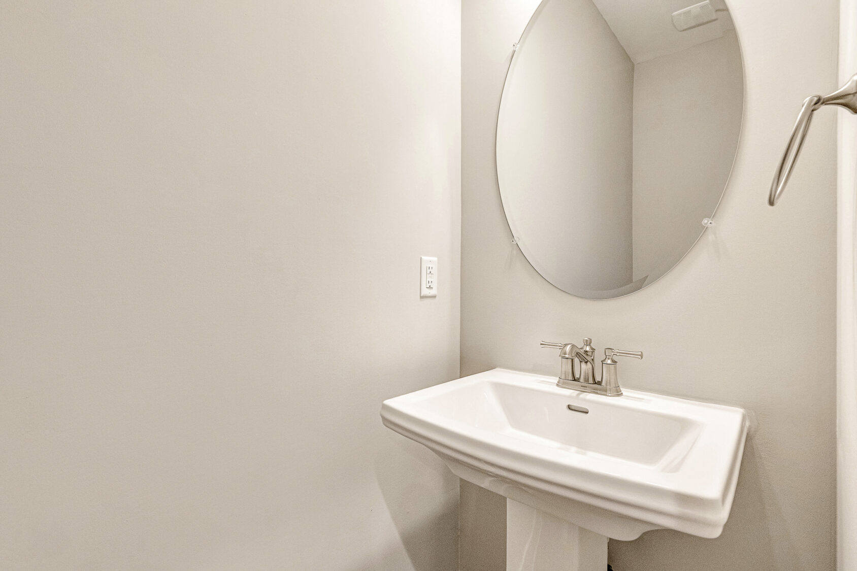 A white pedestal sink with a round mirror above it adds style to the minimalist Somerset Hill Lot 7 bathroom.