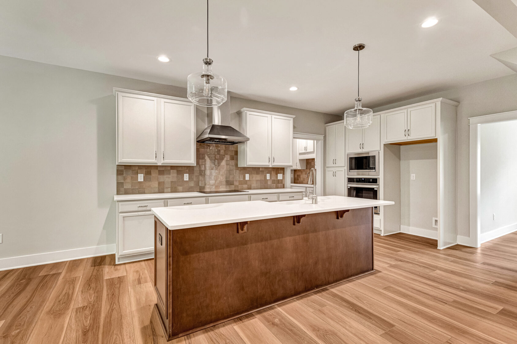 Modern Somerset Hill kitchen with white cabinets, large island, wood floors, and stainless steel appliances. Lot 7.