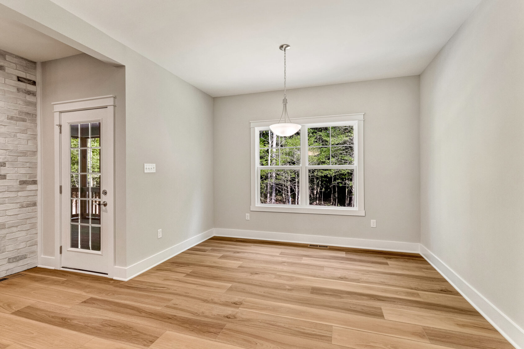 Empty room at Somerset Hill, Lot 7 features light wood floors, white walls, a window, and door to the outside.