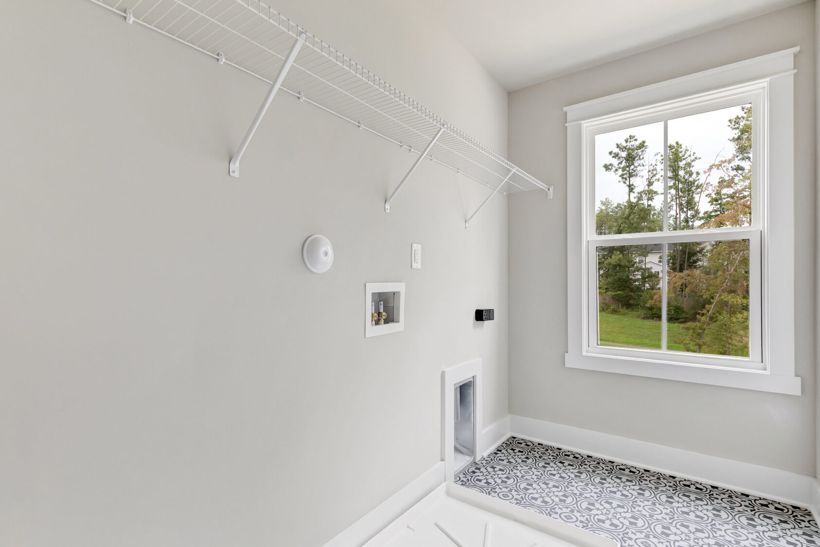 Lot 20 Somerset Hill: Empty laundry room with white wire shelf, patterned tile, window, and washer-dryer hookups.