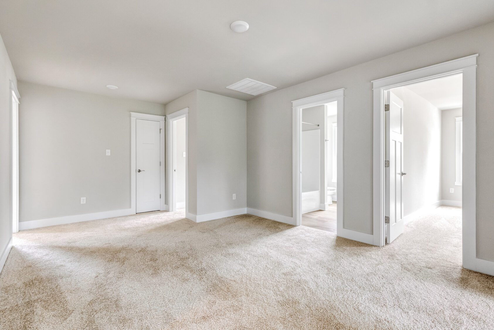 Empty beige carpeted room with white walls, three doorways, and natural light—located in Somerset Hill’s Lot 20.