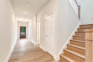 Bright hallway in Somerset Hill with light wood floors, white doors, and stairs; door with window at Lot 20′s end.