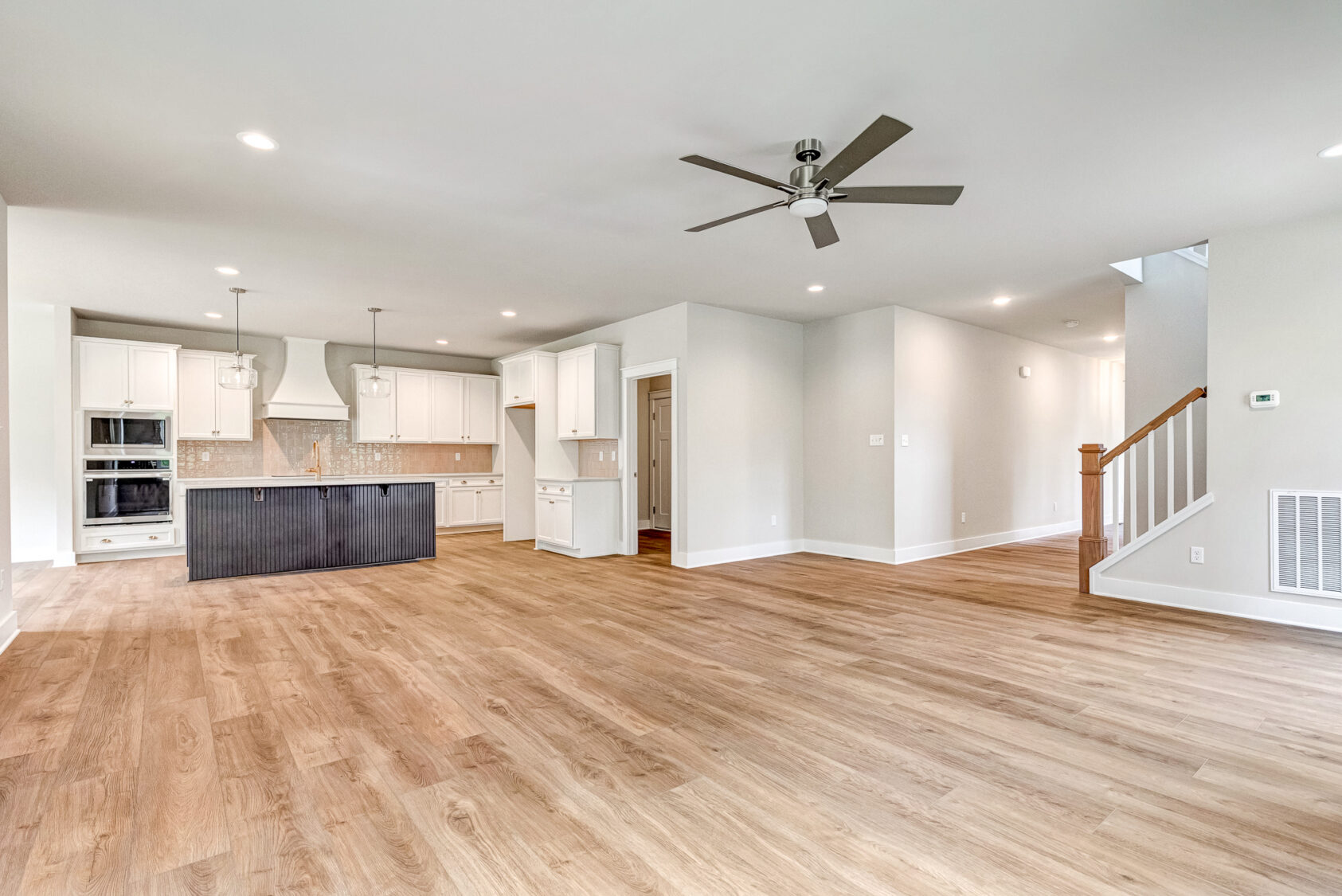 Spacious open-concept living area at Lot 20 Somerset Hill with wood floors, white kitchen, island, ceiling fan, and stairs.