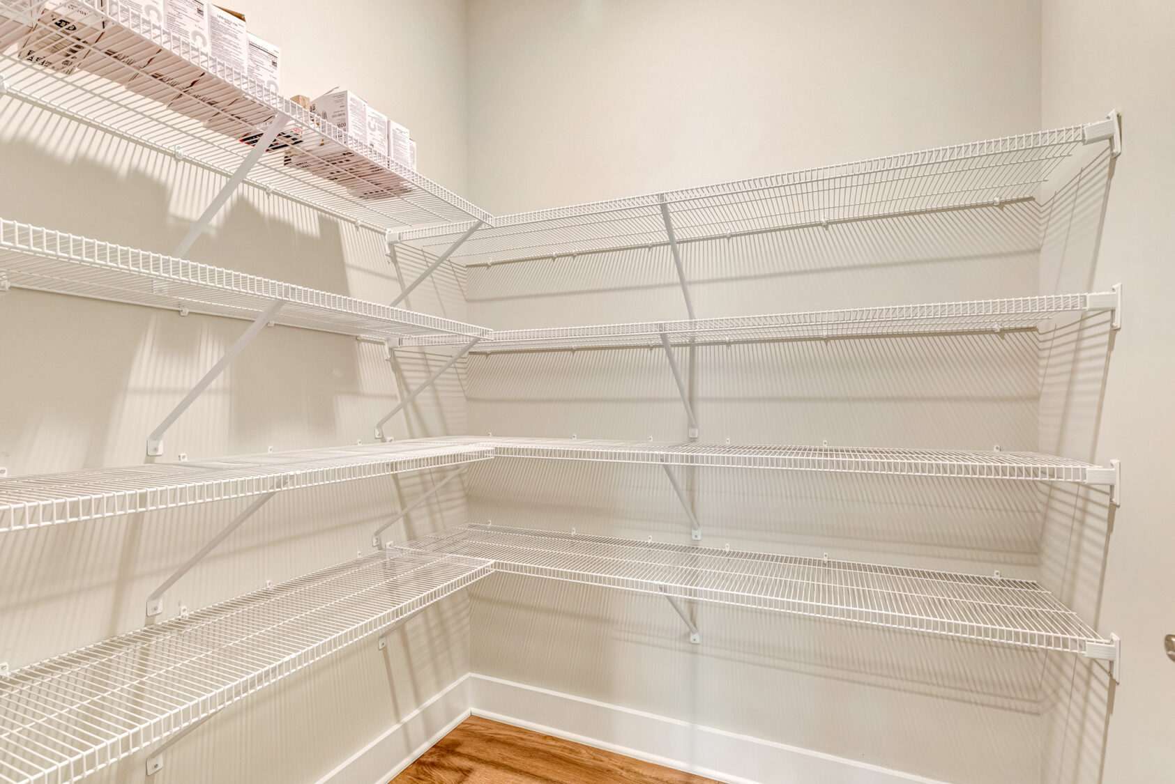 Lot 20 Somerset Hill: Empty pantry with white wire shelves, beige walls, wood floor, and boxes on the top left shelf.