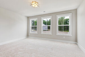 Bright empty room in Somerset Hill with three large windows, beige carpet, and a modern ceiling light fixture.